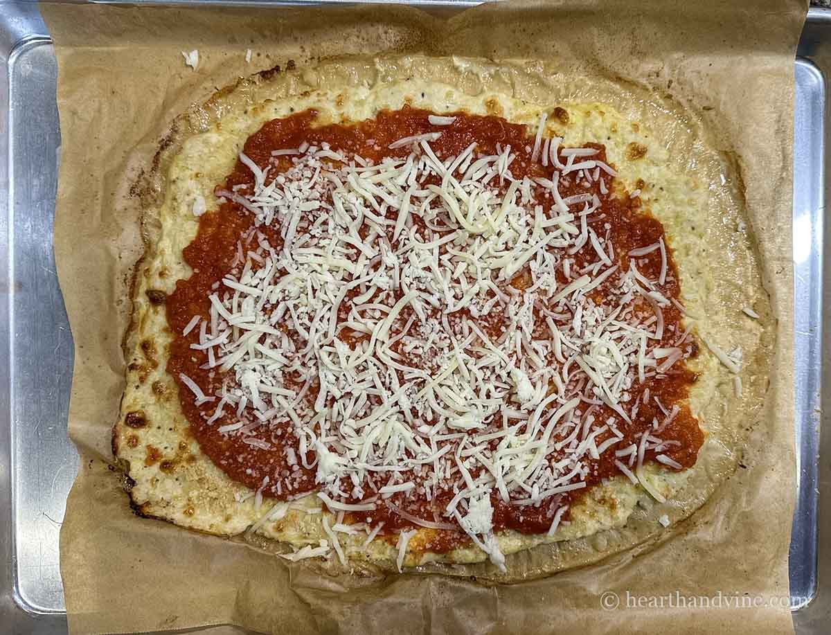 Chicken parm pizza crust with marinara and shredded cheese on top.