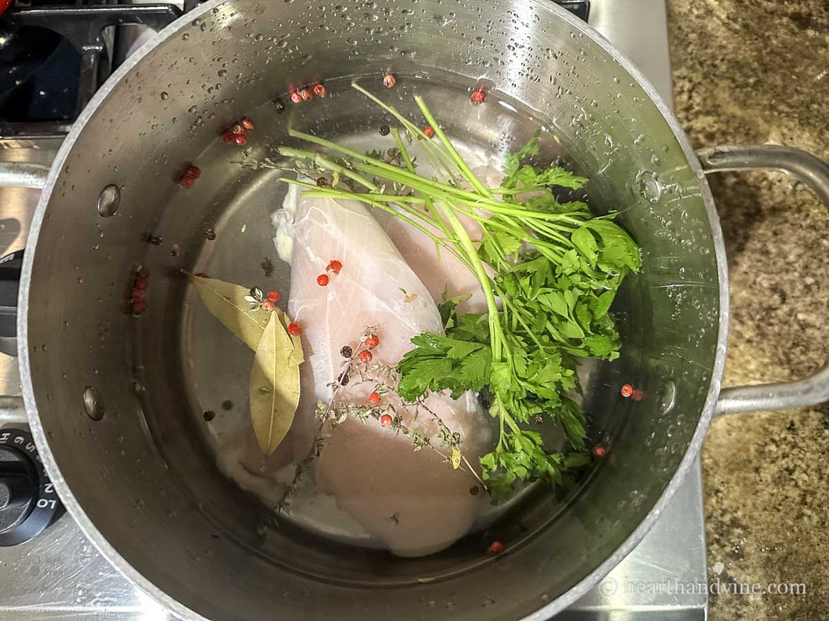 Chicken breasts in a pot of water with peppercorns, parsley and bay.
