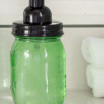 A green glass foaming soap dispenser on a bathroom vanity.