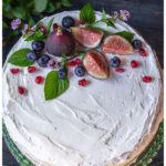 Aerial view of a naked cake with white icing, figs, berries and mint leaves.