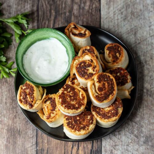 Plate of chicken pinwheels with a bowl of ranch dressing on the side.