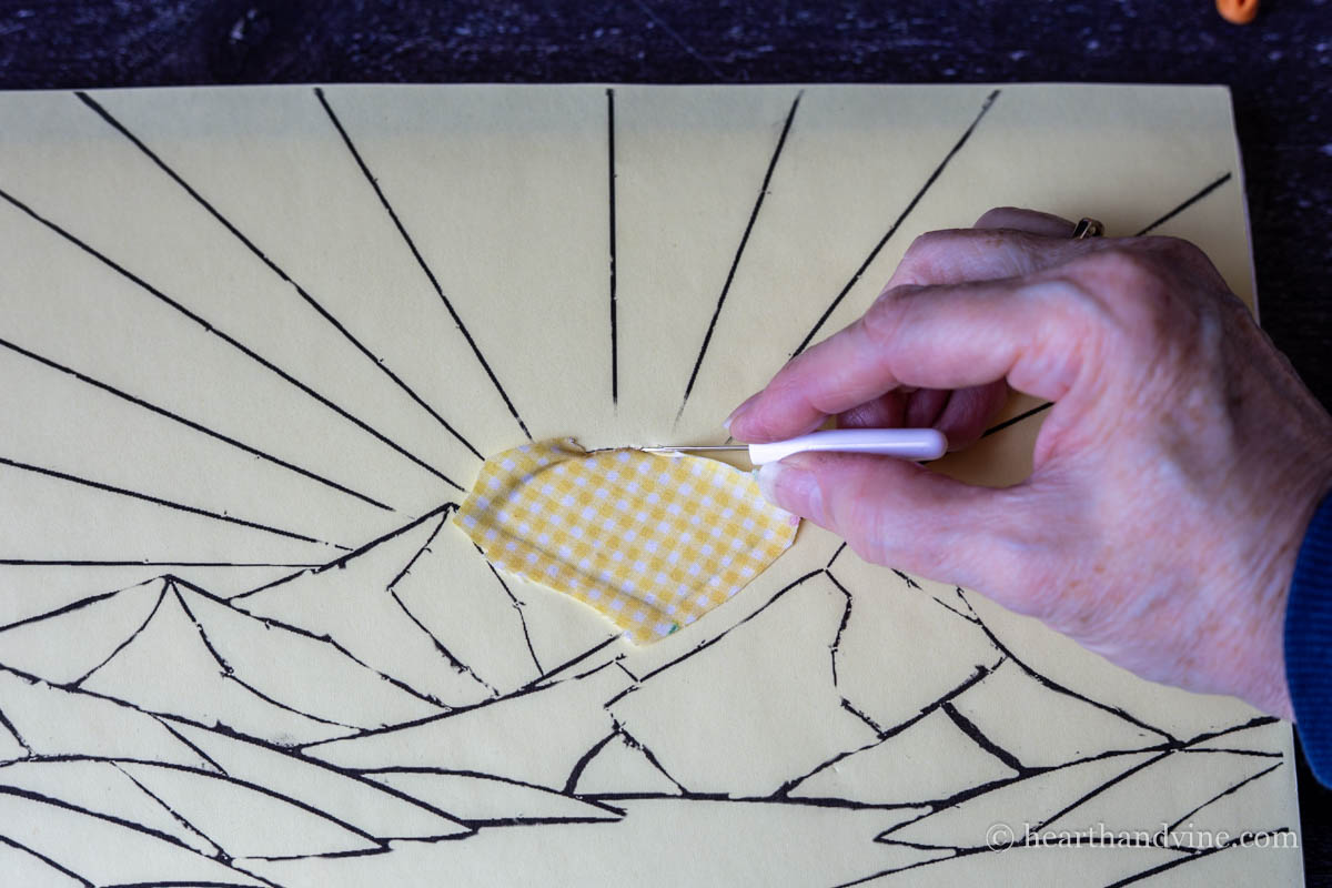 The backside of a seam ripper pressing the edged of the fabric into the foam board.
