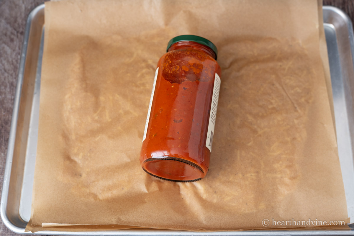 A large jar of marinara sauce rolling out the chicken mixture between two pieces of parchment paper.