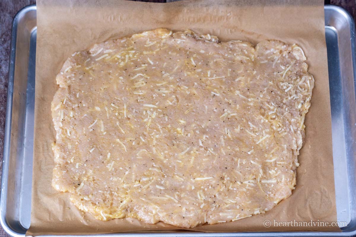 Ground chicken mixture spread out on parchment lined baking pan.