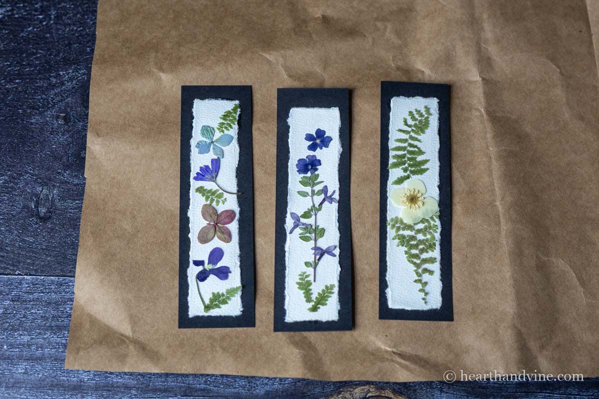 Three pressed flower bookmarks in layout mode on brown craft paper.