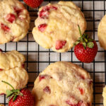 A close up of fresh strawberry cookies on a rack with a few fresh berries.