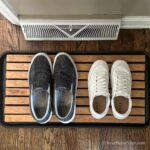 Two sets of shoes on a wooden boot tray in a foyer.