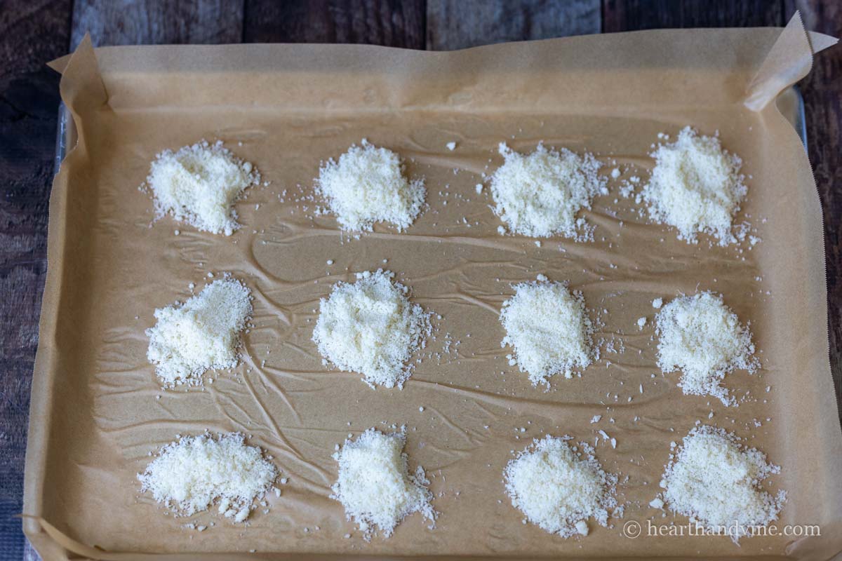 Mounds of grated parmesan cheese on a parchment lined baking tray.