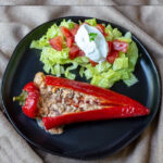 A single stuffed carmen pepper on a plate with lettuce, tomato, and sour cream.