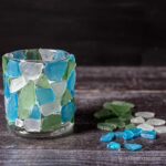 Sea glass candle holder next to blue, green and white sea glass pieces.
