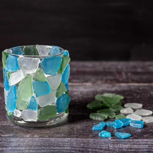 Sea glass candle holder next to blue, green and white sea glass pieces.