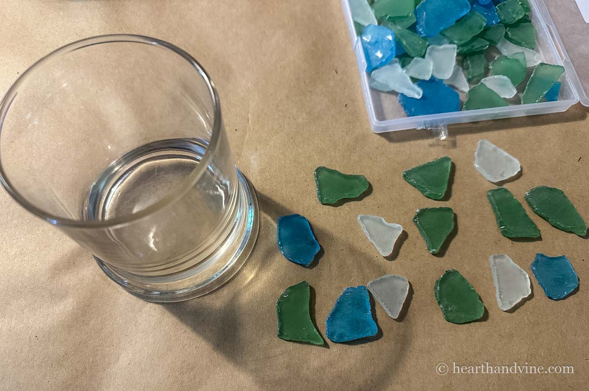A small round clear glass vase, and pieces of sea glass on the side in green, blue and white.