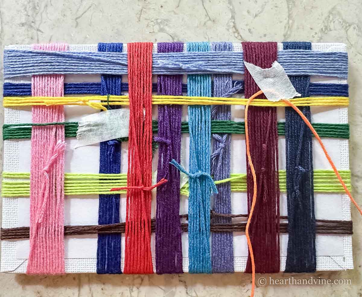 The back of the canvas board during the weaving process showing the tied off threads and tape.