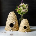 Two decorative bee skeps with a vase of flowers in the background.