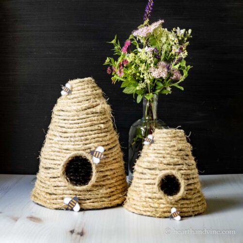 Two decorative bee skeps with a vase of flowers in the background.