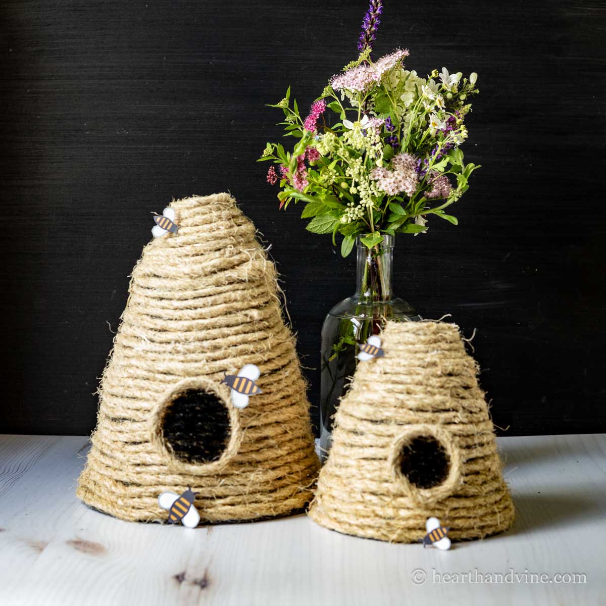 Two decorative bee skeps with a vase of flowers in the background.