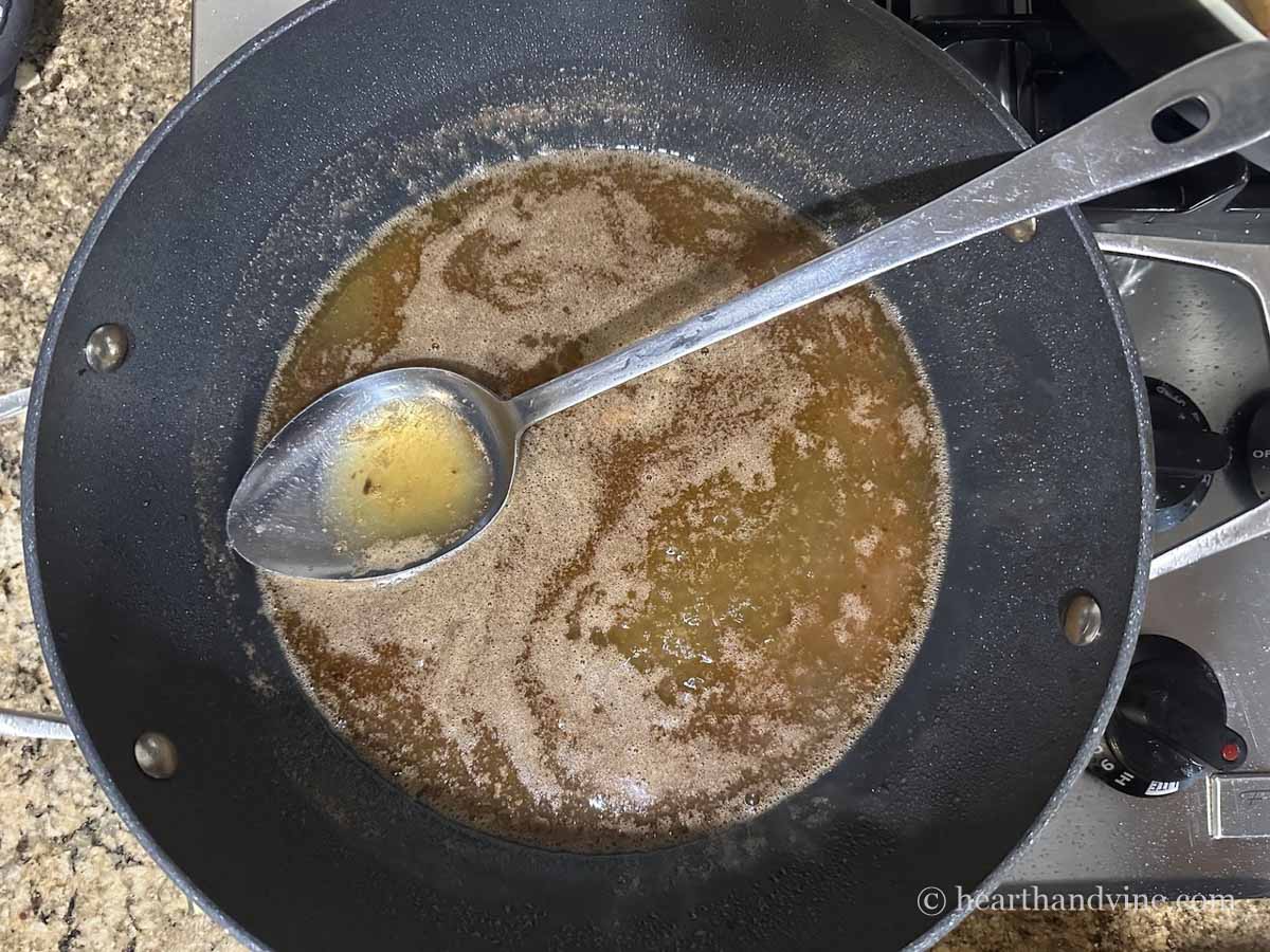 Large skillet with large spoon and sauce of butter, oil, lemon juice and broth.