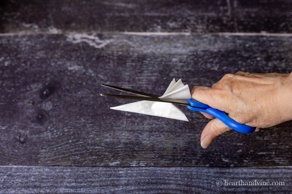 Scissors cutting a curve on the folded coffee filter.