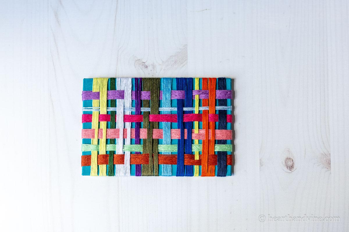 Completed off loom weaving with a blue background and multiple weaved threads.