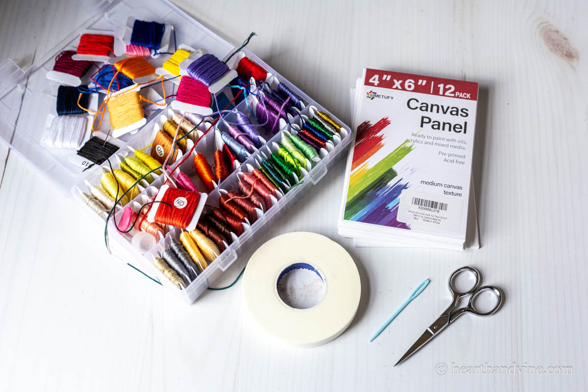Supplies for off loom weaving including embroidery thread, canvas panels, masking tape, needle and scissors.