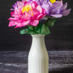 A white milk vase with three colorful coffee filter flowers.