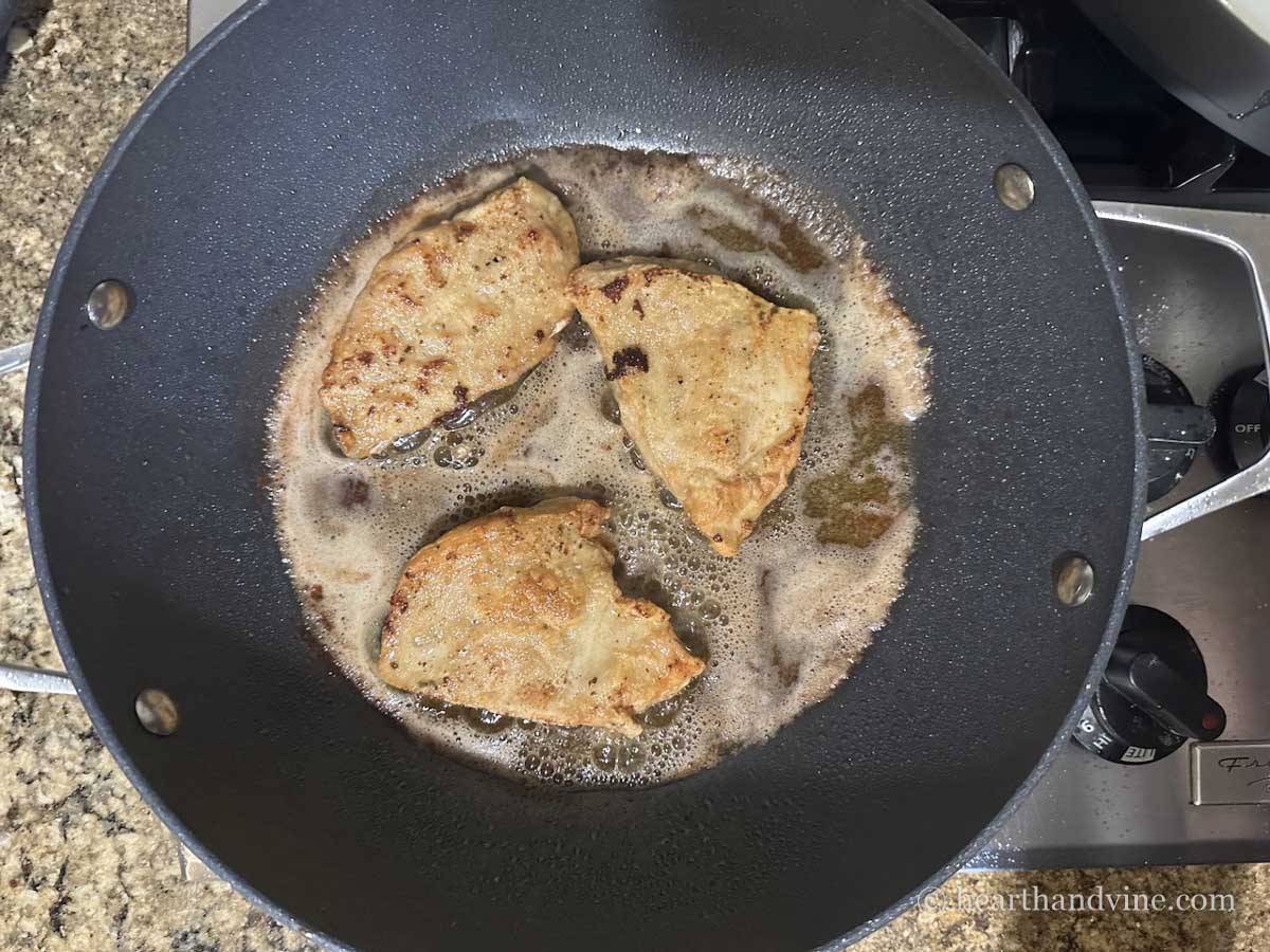 Three chicken breasts browned in butter and olive oil in a skillet.