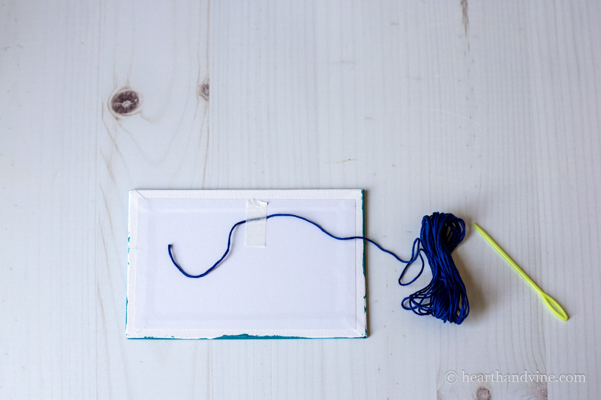 Blue thread taped to the back of a canvas board.