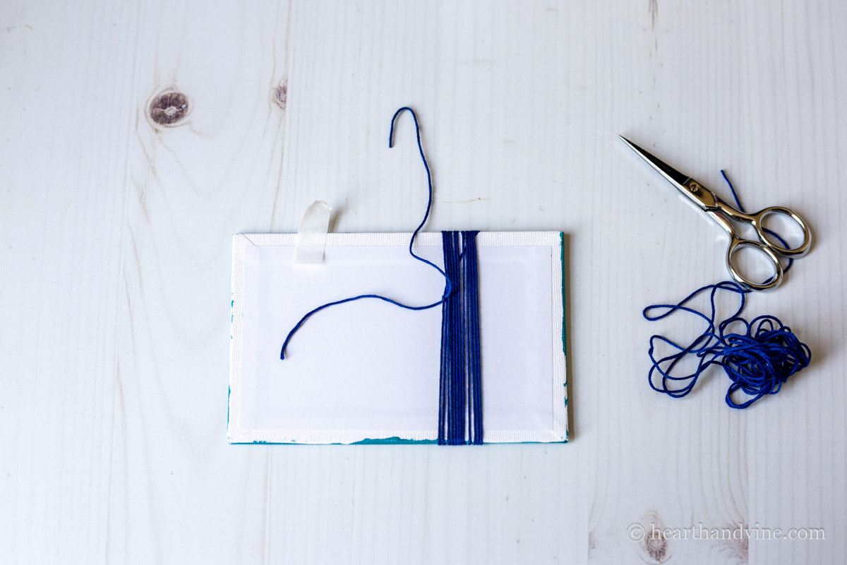 The back of the canvas board after wrapping several blue threads and tying the ends together.