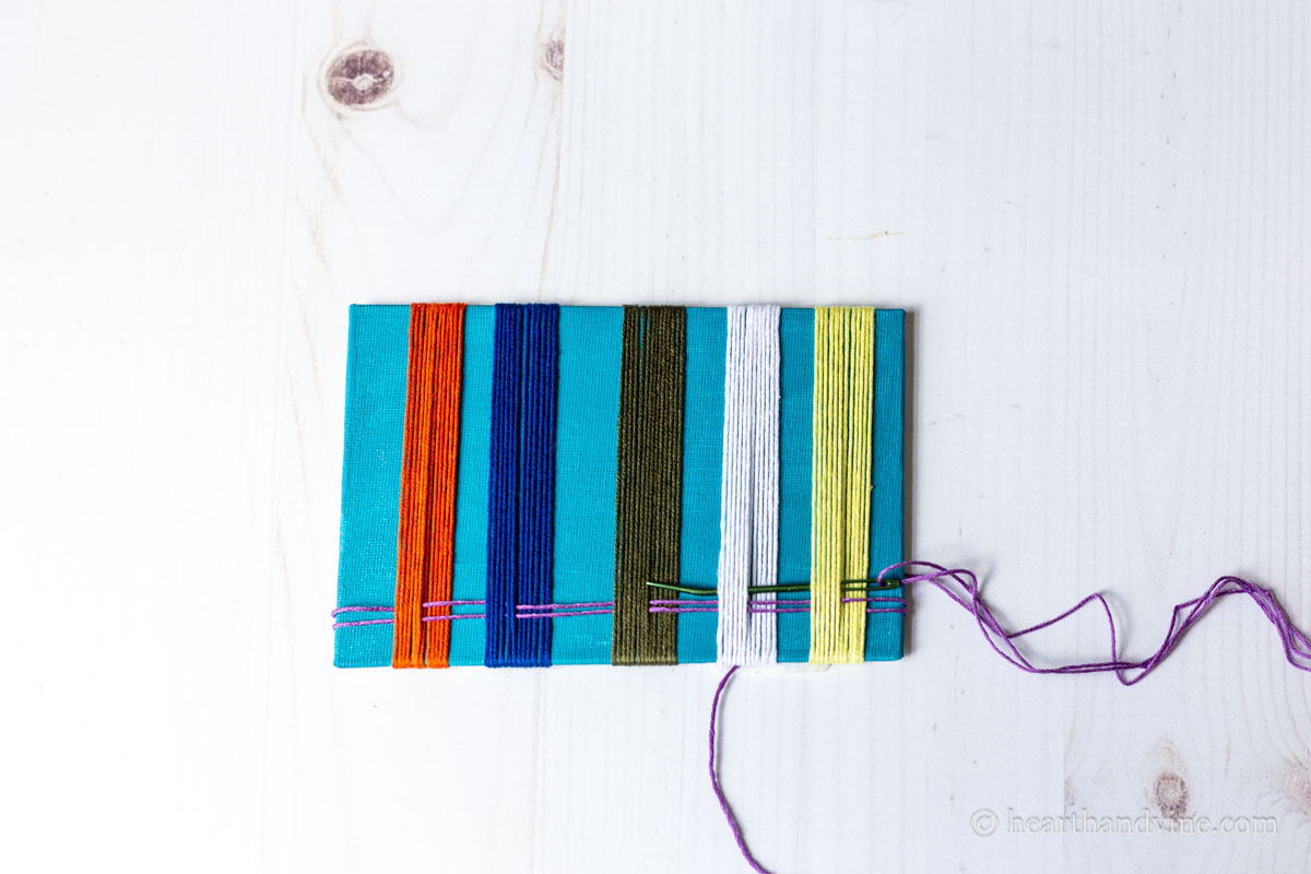 A lavender thread weaving perpendicular to other threads with a large needle.
