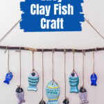 Clay fish in different sizes and colors hanging on a wall from a branch with twine.