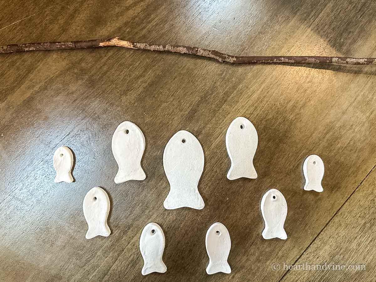 Various sized air dry clay fish in a pattern below a wooden branch.