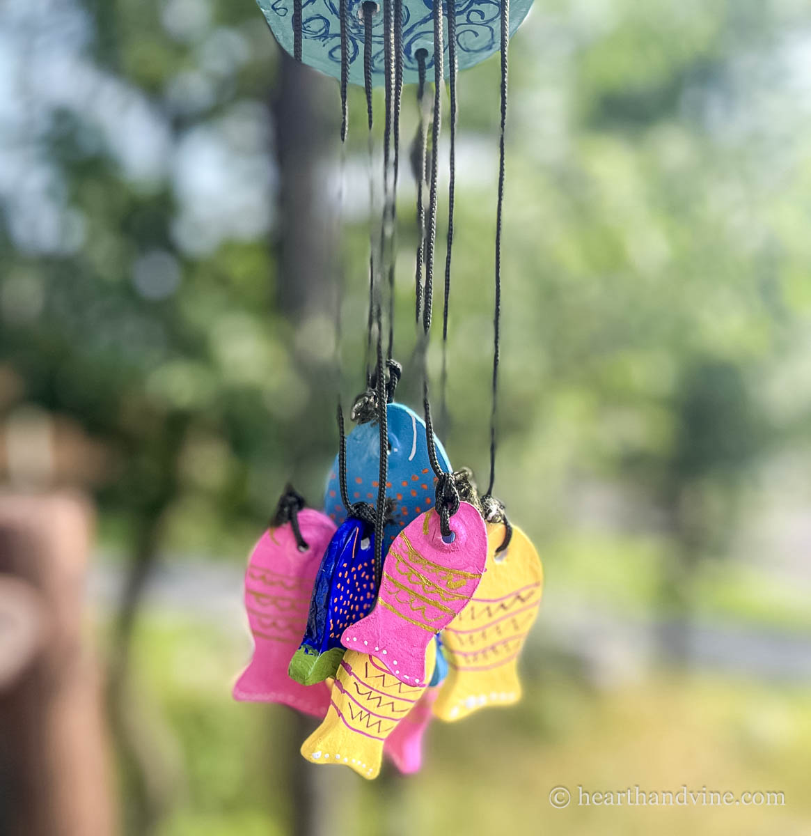 A close look and multiple painted clay fish tied together through a disc in the form of a wind chime.