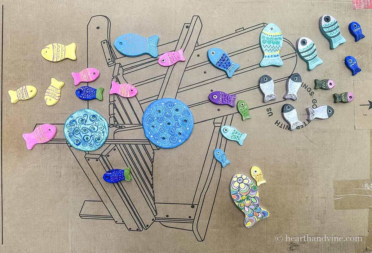 Clay fishes and two discs on a large piece of cardboard after sprayed with polyurethane.