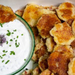 Partial view of small potato pancakes next to a bowl of sour cream & chives.