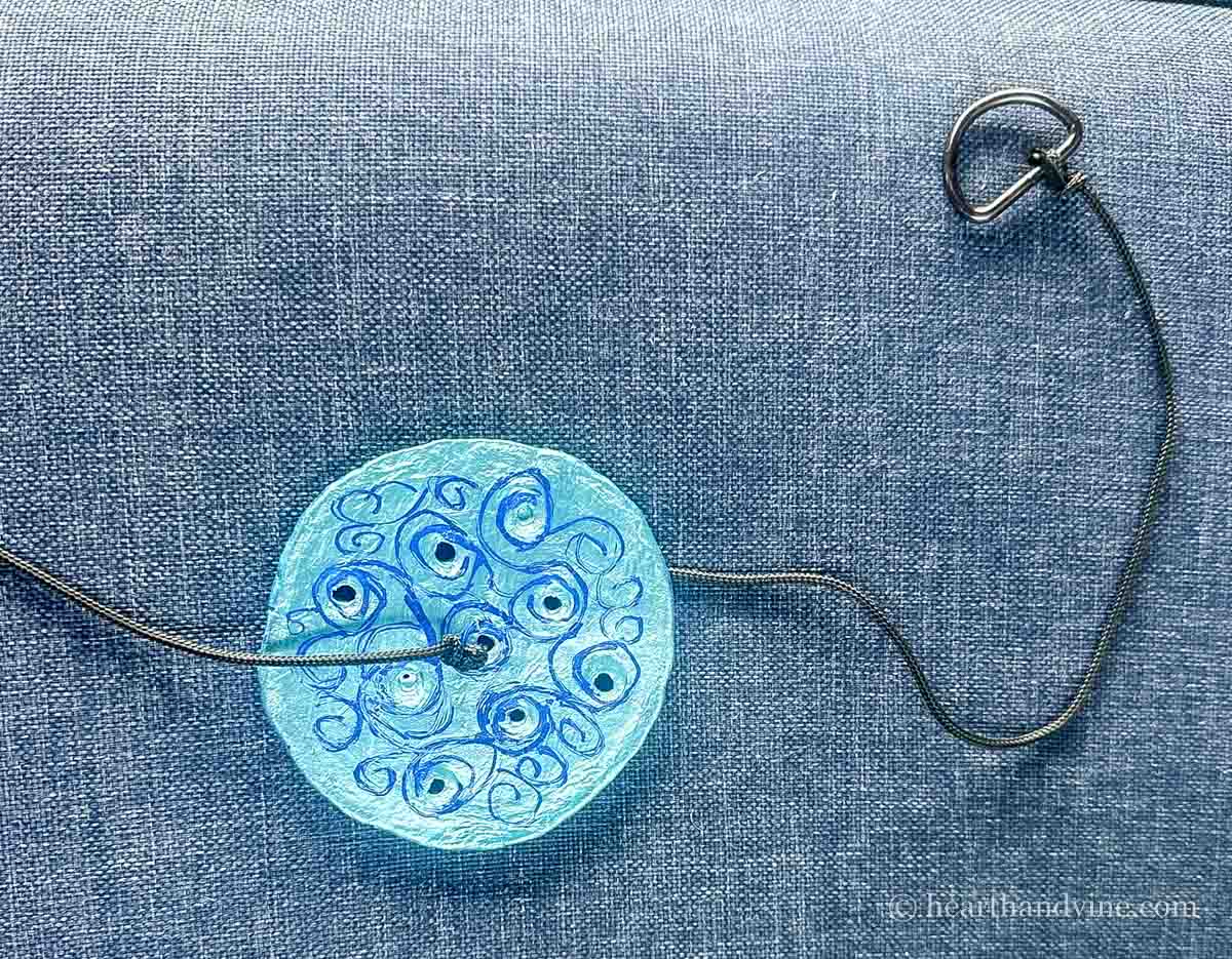 A decorated clay dish tied to a black cord that's tied to a D ring.