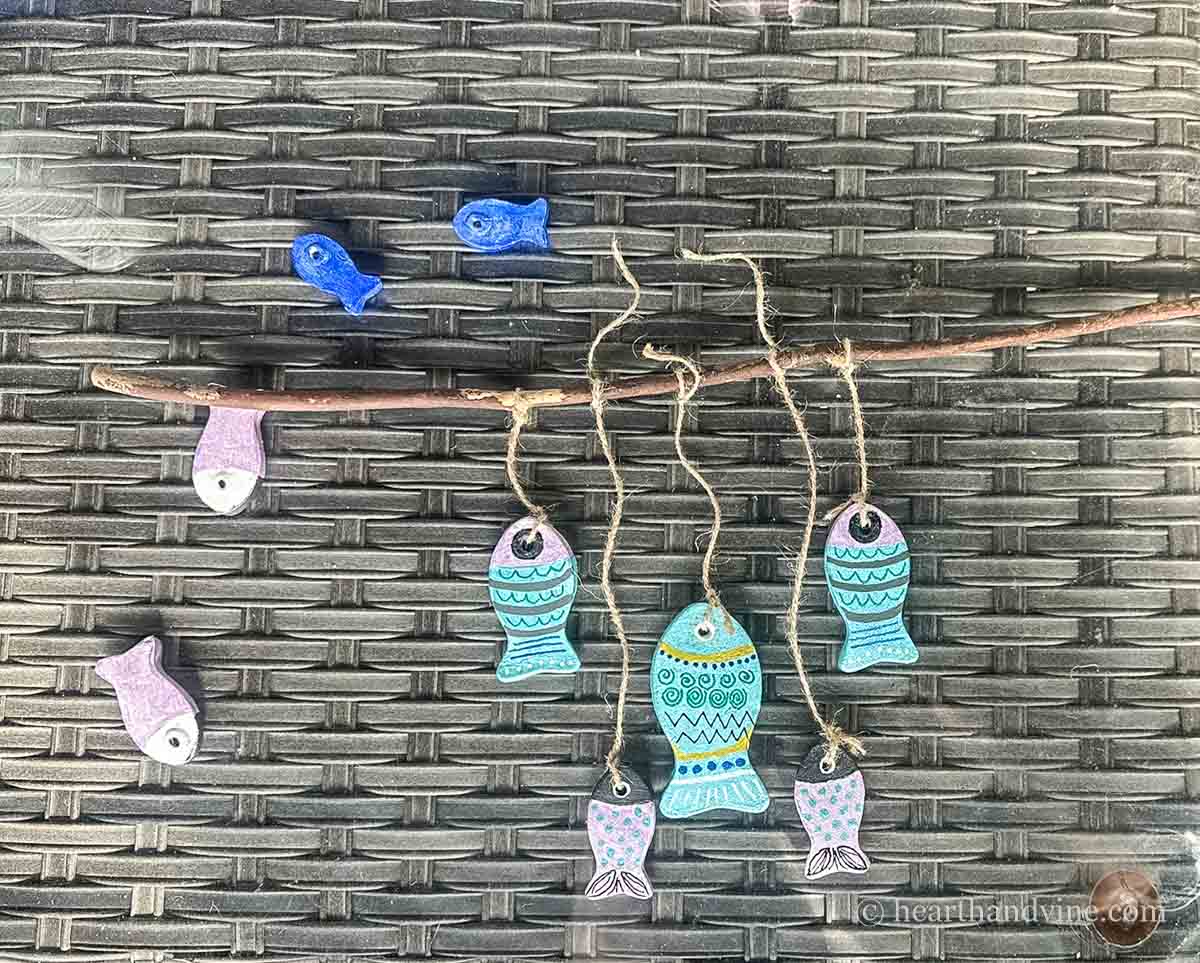 Painted clay fish being tied to a branch with twine.