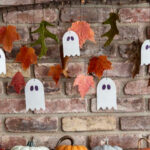 Partial view of a ghost and leaf garland hanging from a branch on a brick wall.