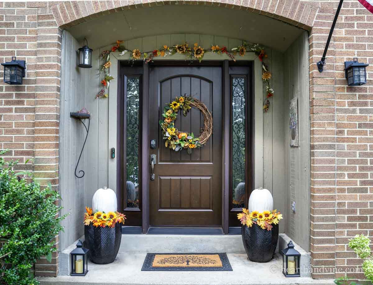 A front porch decorated for fall with sunflowers and pumpkins.