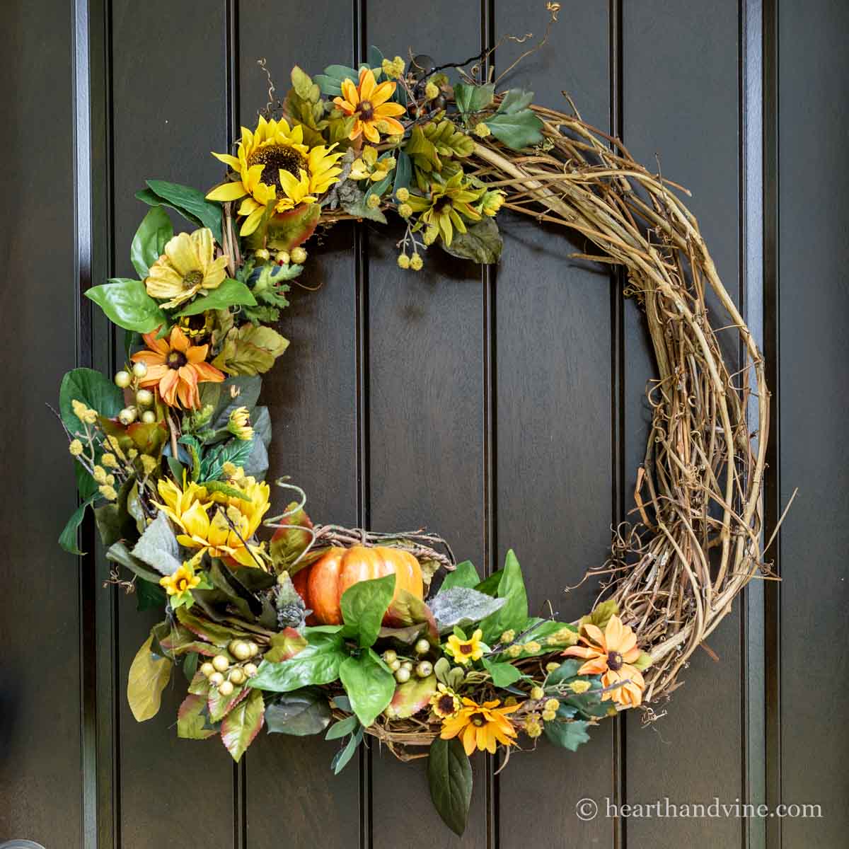 Grapevine wreath partially decorated with sunflowers, a small pumpkin and other green foliage.