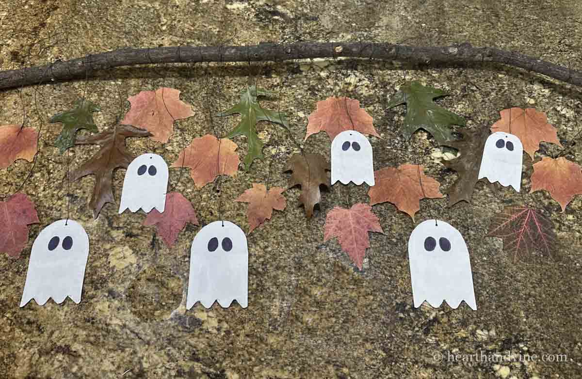 Ghosts and fall leaves tied to a large tree branch lying on a counter.