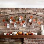 Ghost garland and fall leaves hanging from a branch on a brick wall.