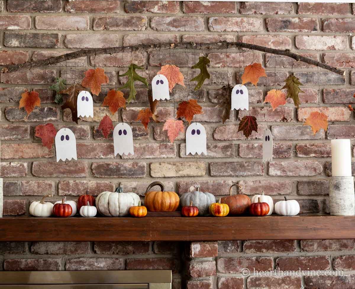 Ghost garland and fall leaves hanging from a branch on a brick wall.