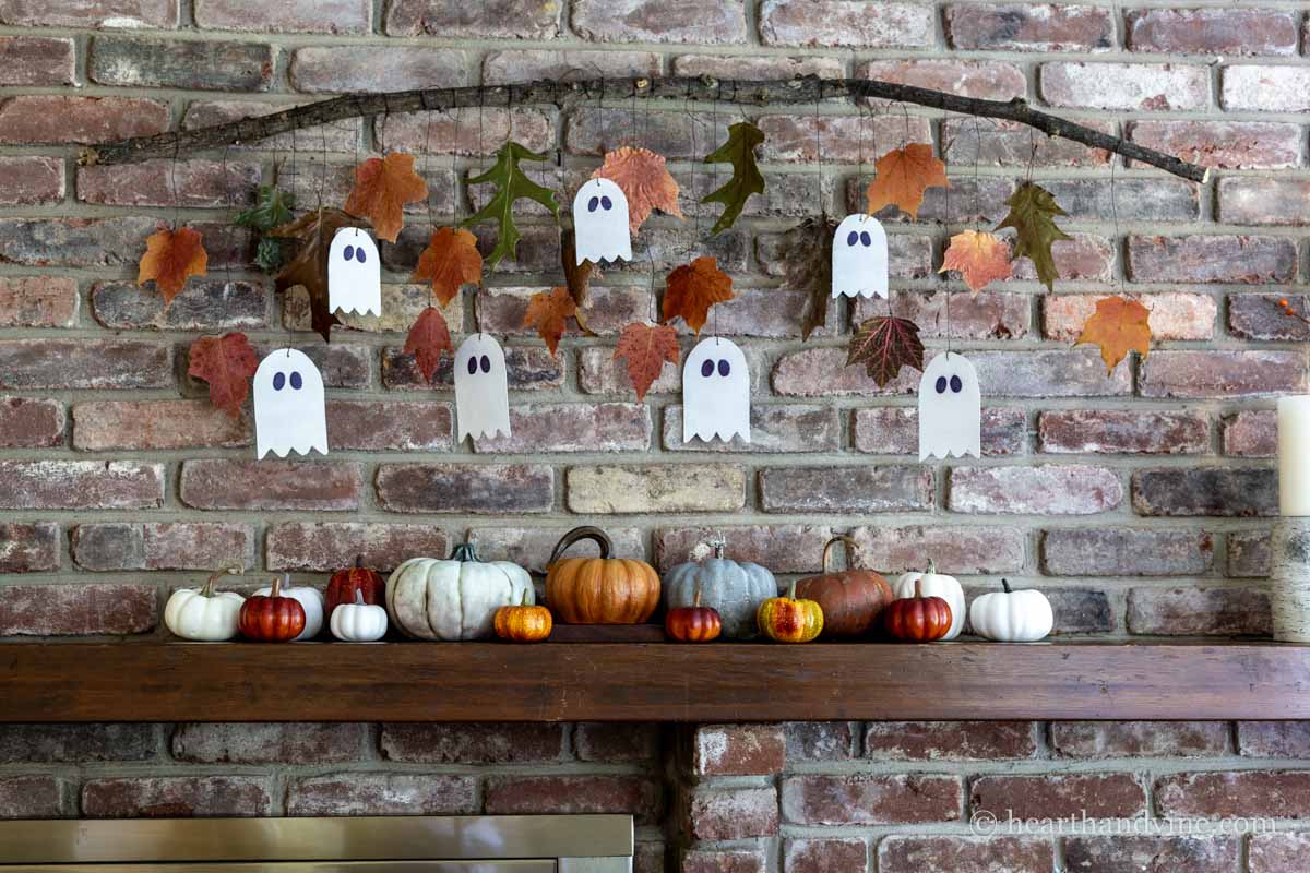 Ghost garland with fall leaves hanging above a mantel with pumpkins below on the mantel.