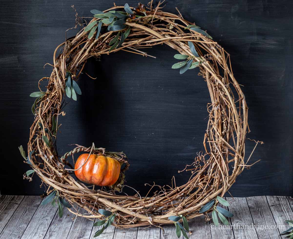 A small artificial pumpkin set into the bottom left of a large grapevine wreath.