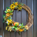 Grapevine wreath with sunflowers and a pumpkin on a front door.