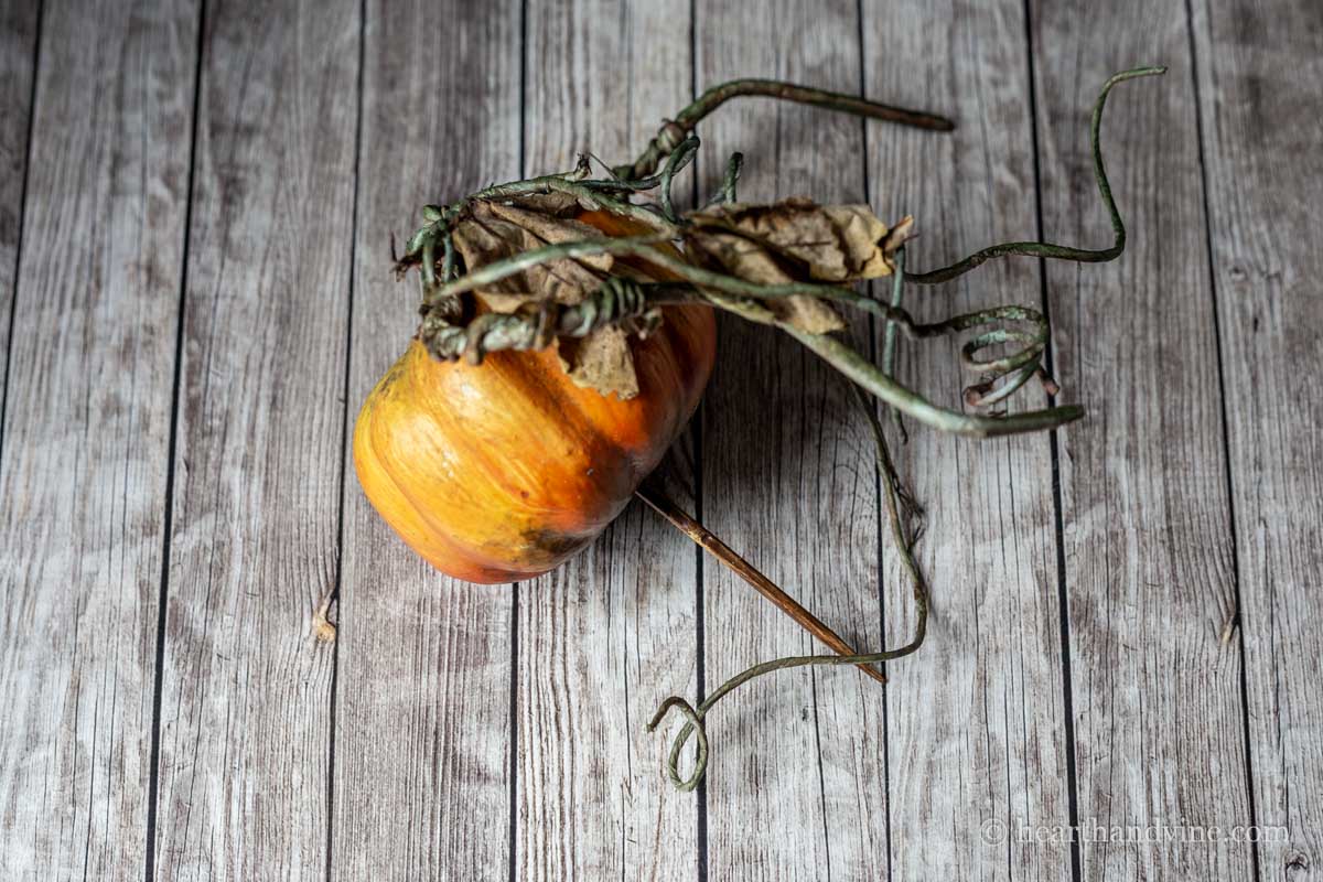 A small faux pumpkin with a brown wooden skewer in the bottom.