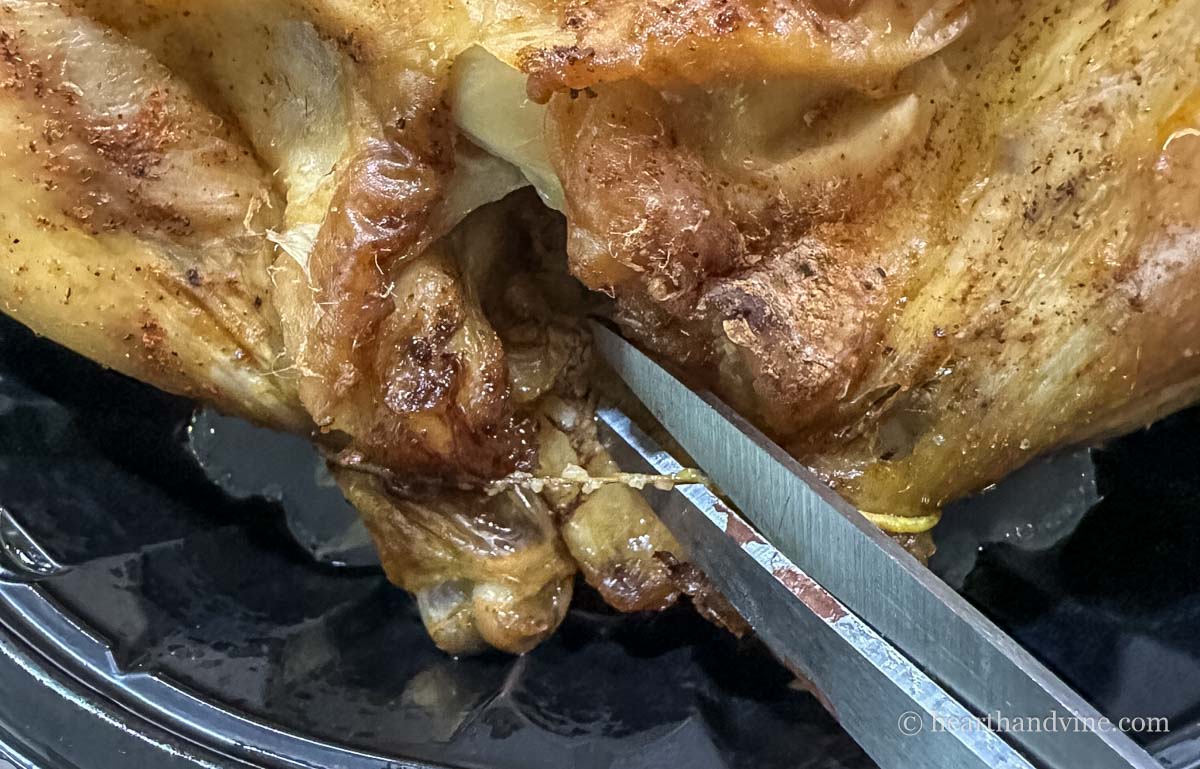 Scissors cutting the binding string from the rotisserie chicken.