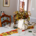 Thanksgiving table decorations including a floral pumpkin centerpiece, leaf runner, leaf place cards and acorn napkin ties.