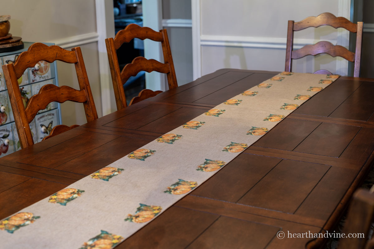 Pumpkin napkin decorations on a fabric table runner in the center of a long dining table.