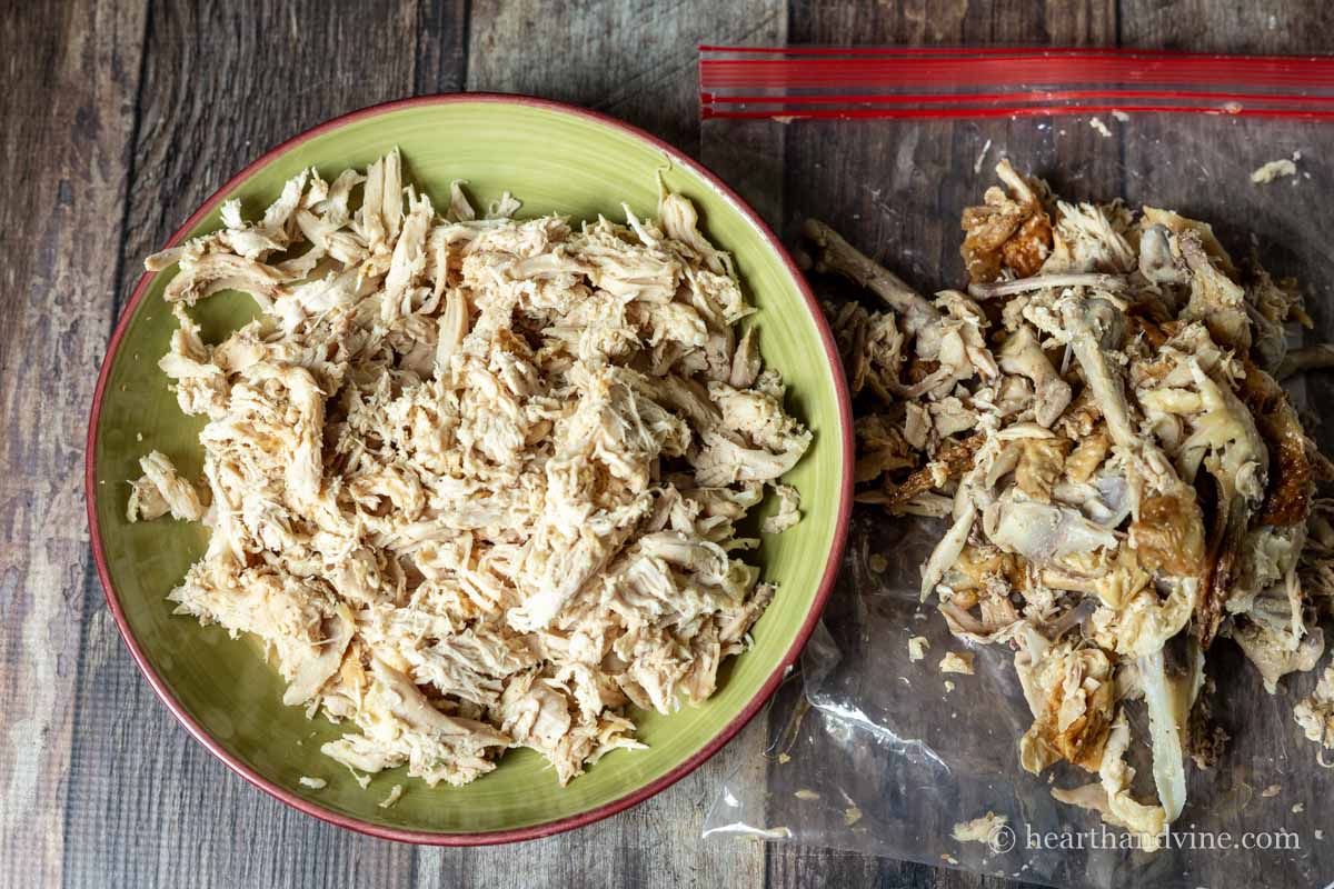 Bowl with shredded rotisserie chicken next to a bag with skin and bones.